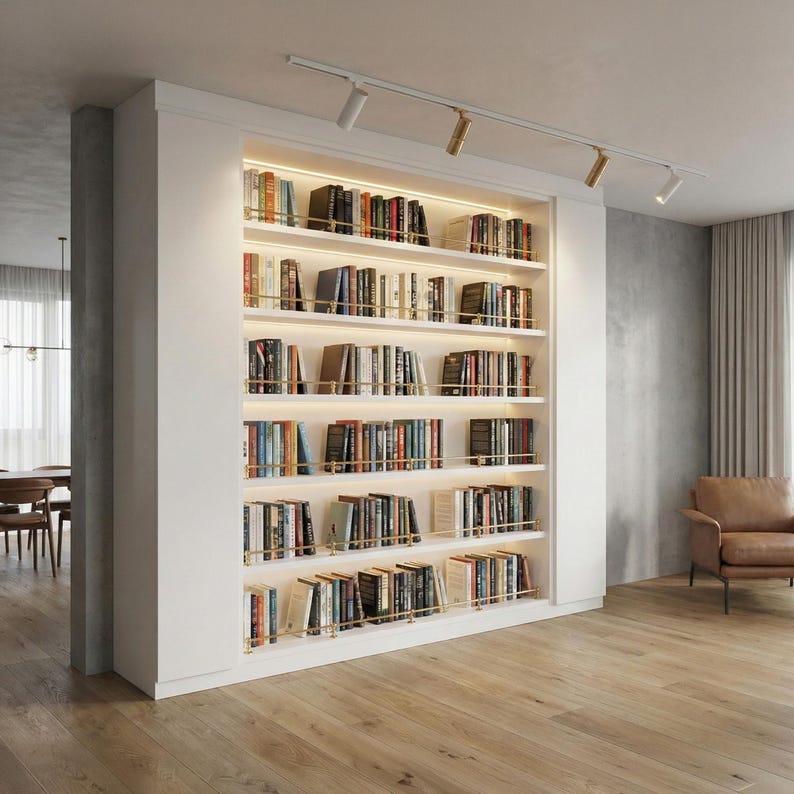 May include: A built-in white bookshelf filled with books of various sizes and colors. The shelves are illuminated with warm lighting, and accented with brass-colored rods. The bookshelf is a prominent feature in a modern living space.