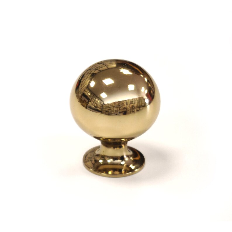 May include: A polished brass cabinet knob with a spherical design. The knob has a reflective surface, and a circular base. The knob is designed for use on drawers, cabinets, or other furniture.