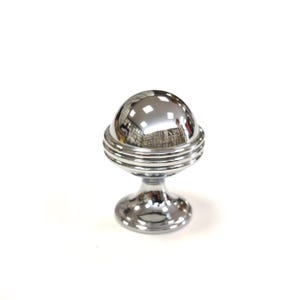 May include: A shiny, chrome-finished cabinet knob with a spherical top and a pedestal base. The spherical top has a reflective surface, and the base has a circular design. The knob is designed for furniture and home decor.