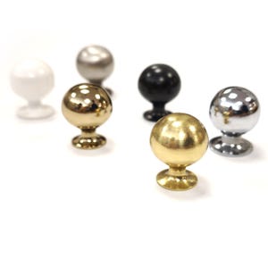 May include: A selection of spherical cabinet knobs in different finishes. The knobs have a base and come in white, silver, black, and gold. These knobs are suitable for furniture and home decor projects.