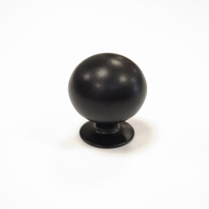 Op de afbeelding: Zwarte, bolvormige kastknop met een matte afwerking. De knop staat op een korte, cirkelvormige basis. De hardware is ontworpen voor laden, kasten of andere meubels. De knop heeft een eenvoudig, maar elegant ontwerp.
