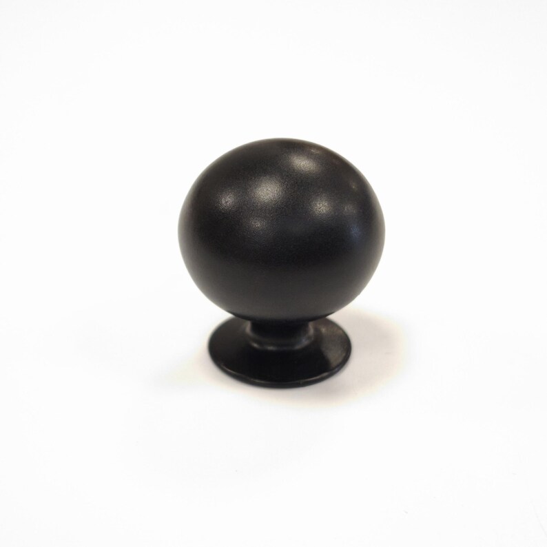 Op de afbeelding: Zwarte, bolvormige kastknop met een matte afwerking. De knop staat op een korte, cirkelvormige basis. De hardware is ontworpen voor laden, kasten of andere meubels. De knop heeft een eenvoudig, maar elegant ontwerp.