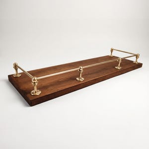 May include: A rectangular, dark brown wooden shelf with brass-colored metal railings. The shelf has a simple, elegant design, with the metal supports and railings adding a touch of sophistication. The shelf is ideal for displaying items.