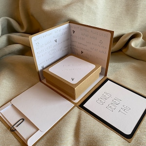 Könnte beinhalten: Eine braune und weiße Pop-up-Karte mit einer kleinen Box im Inneren. Die Karte hat den Text "Happy Birthday" und "Hip Hip Hurra" auf der Vorderseite. Die Box hat den Text "Für Dich Von Herzen" auf der Oberseite. Die Karte ist geöffnet und die Box ist sichtbar. Die Karte hat auch den Text "Genieß Deinen Tag" auf der Innenseite.