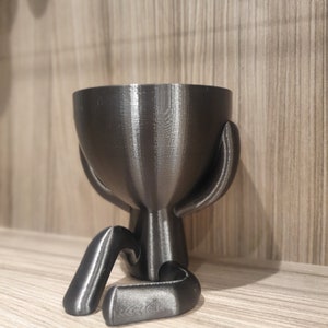 May include: A black 3D printed planter shaped like a person sitting with their legs crossed. The planter has a smooth, shiny finish.