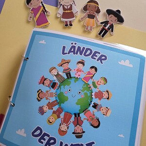 Könnte beinhalten: Ein blaues und weißes Buch mit dem Titel "Länder der Welt" und einer bunten Illustration von Kindern aus verschiedenen Ländern, die sich an den Händen um einen Globus halten. Das Buch hat einen Ringbinder und ist mit Wolken verziert.