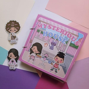 Könnte beinhalten: Ein rosa Notizbuch mit den Worten "MYSTERIOUS HOUSE" und Cartoon-Illustrationen von Menschen und Tieren. Zwei transparente Aufkleber von Cartoon-Charakteren befinden sich links. Das Notizbuch hat Metallringe.