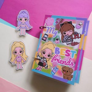 Könnte beinhalten: Ein farbenfrohes Notizbuch mit dem Text "My BEST friends" und Cartoon-Illustrationen von Mädchen, Make-up und einem Hund. Zwei puppenartige Aufkleber von Mädchen sind ebenfalls vorhanden, einer mit lila Haaren und der andere mit blonden Haaren.