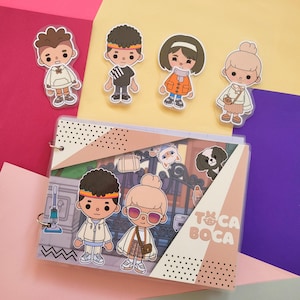 Peut inclure: Un classeur coloré avec un logo Toca Boca et divers autocollants de personnages de dessins animés. Les autocollants comprennent une fille aux cheveux bruns portant une veste rouge, un garçon aux cheveux bruns portant une chemise noire, une fille aux cheveux blonds portant une chemise blanche, un garçon aux cheveux bruns portant une chemise blanche et une fille aux cheveux blonds portant une chemise blanche.