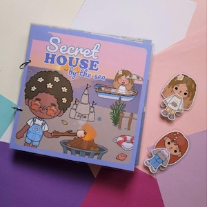 Può includere: Un libro di attività rilegato a spirale con il titolo "Secret House by the Sea" e illustrazioni di cartoni animati. La copertina presenta un personaggio che arrostisce un marshmallow. Sono visibili anche due bambole adesive.