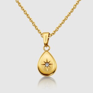 May include: A gold-toned necklace featuring a teardrop-shaped pendant. The pendant has a smooth, polished surface with a central starburst engraving that holds a single, small, clear, round-cut gemstone at its centre, suspended on a link chain.
