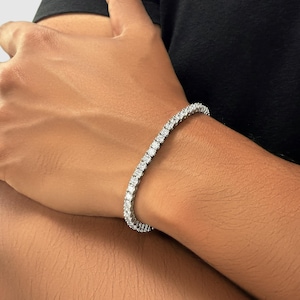 Könnte beinhalten: Ein Tennisarmband mit einer Reihe von runden, weißen Edelsteinen, die in einem silberfarbenen Metall gefasst sind. Das Armband wird am Handgelenk getragen und zeigt sein elegantes Design und seinen Glanz. Ein klassisches Schmuckstück.