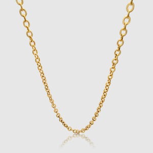 Könnte beinhalten: Eine goldfarbene Halskette mit einem filigranen, verbundenen Design. Die Halskette wird vor einem hellen Hintergrund präsentiert, mit einer subtilen Reflexion darunter sichtbar. Die Kette besteht aus kleinen, gleichmäßig verteilten Gliedern.