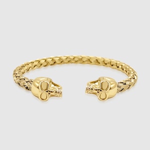 Op de afbeelding: Een gouden gevlochten armband met schedelvormige eindkappen.
