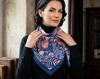 May include: A square silk scarf with a navy blue border and a vibrant floral pattern in shades of orange, pink, and white on a blue background. The scarf is worn around the neck, showcasing its intricate design and color palette.