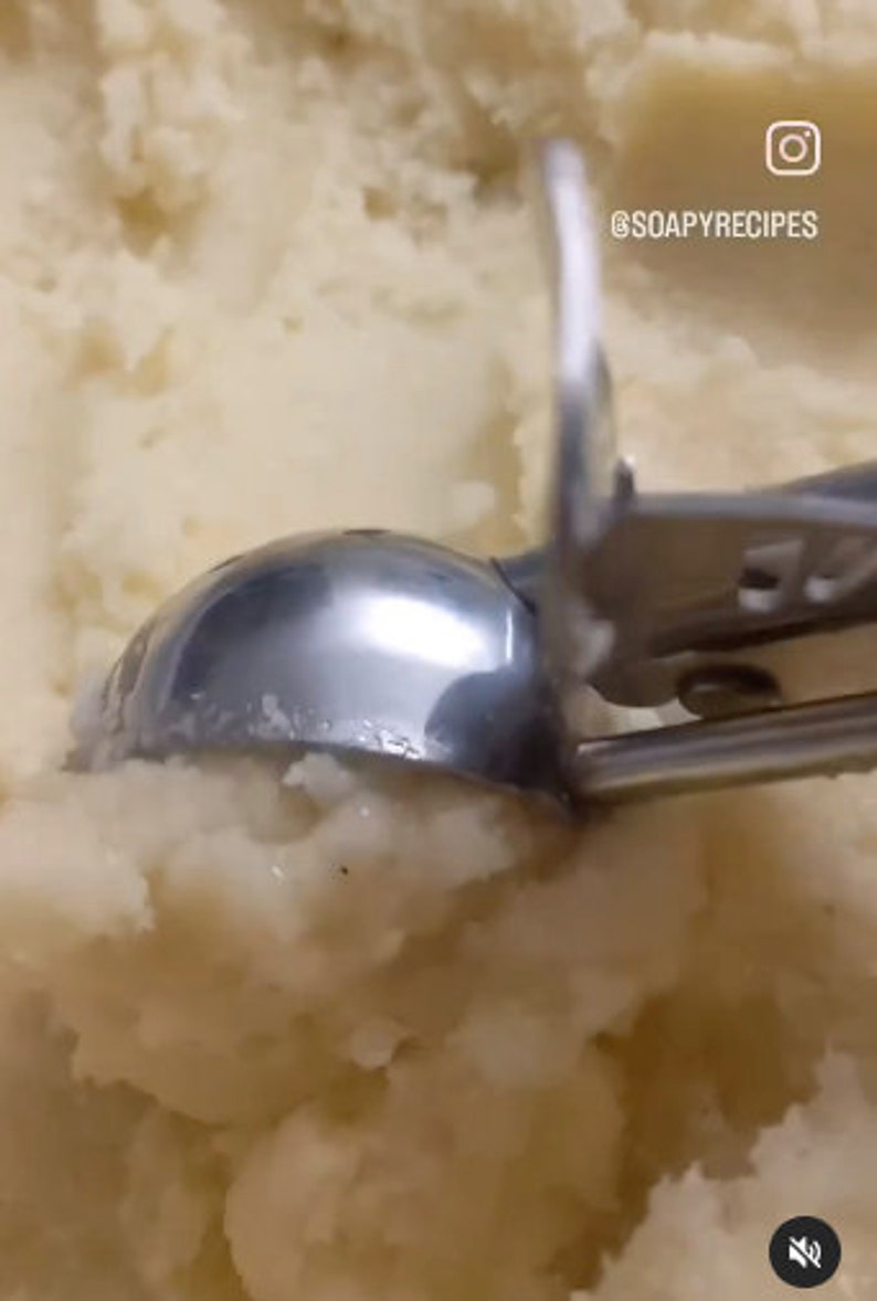 Op de afbeelding: Een close-up van een zilveren ijsbollepel die een grote kom met aardappelpuree opschept. De lepel is gedeeltelijk ondergedompeld in de puree, en de steel is zichtbaar op de achtergrond. De tekst "@SOAPYRECIPES" is zichtbaar in de rechterbovenhoek van de afbeelding.