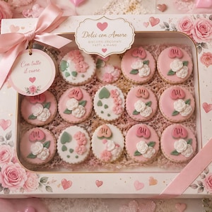 Pode incluir: Uma caixa de presente retangular contendo quinze biscoitos redondos decorados com glacê rosa e branco, detalhes florais e corações. A caixa apresenta uma fita rosa, uma etiqueta circular com Con tutto il cuore e o texto Dolci con Amore.