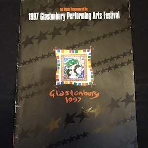 May include: A black programme cover for the 1997 Glastonbury Performing Arts Festival. The cover features the text "The Official Programme of the 1997 Glastonbury Performing Arts Festival" and "Glastonbury 1997". The cover is decorated with star patterns.