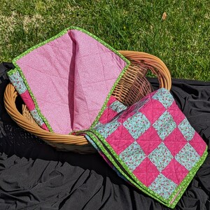 May include: Two pink and green patchwork quilts with floral patterns. The quilts are folded and placed in a wicker basket.