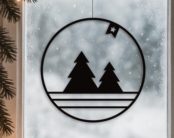 May include: Black metal Christmas ornament featuring a circular design with two stylized fir trees and a star. The ornament hangs in front of a frosted window, evoking a winter scene. The design includes horizontal lines at the bottom of the circle.