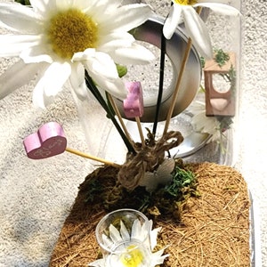 May include: A clear glass jar with a white lid, filled with a floral arrangement of white daisies and pink hearts. The jar is sitting on a brown coir mat.