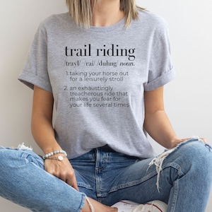May include: A gray t-shirt with the text "trail riding" defined as "taking your horse out for a leisurely stroll" and "an exhaustingly treacherous ride that makes you fear for your life several times".