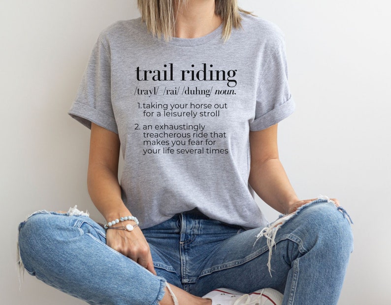 May include: A gray t-shirt with the text "trail riding" defined as "taking your horse out for a leisurely stroll" and "an exhaustingly treacherous ride that makes you fear for your life several times".