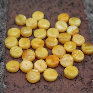 May include: A collection of round, yellow amber beads with a hole in the centre. The beads are smooth and polished.