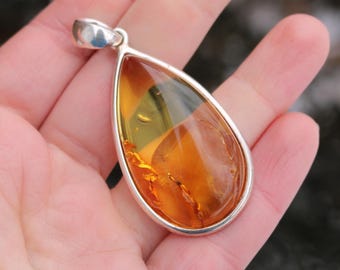May include: A teardrop-shaped amber pendant set in a silver frame. The amber is a rich, golden color with visible inclusions.