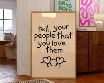 Pode incluir: Uma impressão artística retangular emoldurada com fundo bege claro, apresentando o texto preto "tell your people that you love them" acima de dois personagens simples em forma de coração desenhados em linhas pretas de mãos dadas.
