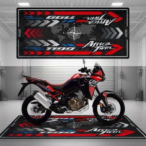 Op de afbeelding: Een rode en zwarte Honda Africa Twin 1100 motorfiets met een zwart-witte wereldkaart en kompasontwerp op de vloermat. De mat heeft ook de tekst "Africa Twin" en "1100" in rood en wit.