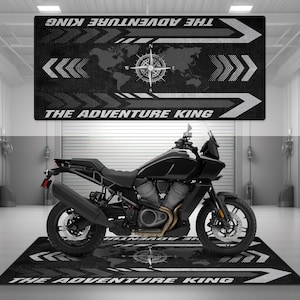 Puede incluir: Una motocicleta negra con un parabrisas y una alfombra de suelo negra y blanca con el texto "THE ADVENTURE KING" en ella.