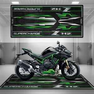 Può includere: Un tappetino per pavimento per moto verde e nero con le parole "H2" e "Supercharge" stampate su di esso. Il tappetino è progettato per proteggere il pavimento da sporco e sporcizia.