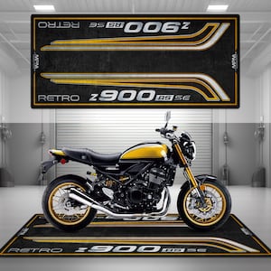 Op de afbeelding: Een zwarte en gele motorfiets met gouden wielen en een zwart-witte vloermat met de tekst "Retro Z900 RS SE" erop gedrukt.