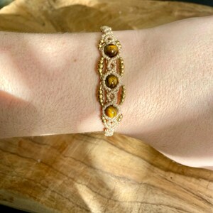 May include: A beige macrame bracelet with gold beads and tiger's eye stones.