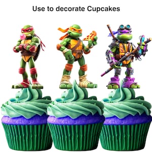 May include: Three cupcakes with green and purple frosting, each topped with a Teenage Mutant Ninja Turtle figurine. The cupcakes have green cupcake liners and the text "Use to decorate Cupcakes" is at the top.
