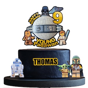 Puede incluir: Un adorno para pastel de Star Wars negro y amarillo con una Estrella de la Muerte, personajes de Lego y el texto "Happy Birthday Young Padawan Thomas".