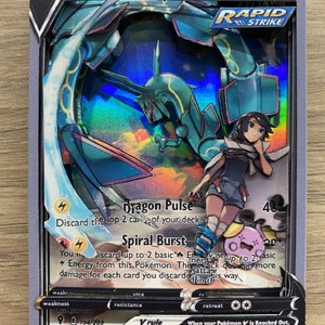 May include: A Pokemon trading card featuring a green and blue dragon Pokemon with a trainer. The card is a basic card with a rapid strike ability. The card has a dragon pulse attack that discards the top 2 cards of your deck and a spiral burst attack that discards up to 2 basic energy cards or up to 2 basic energy cards from this Pokemon. The card has a V rule that states when your Pokemon V is knocked out, your opponent takes 2 prize cards. The card is number 194/203.