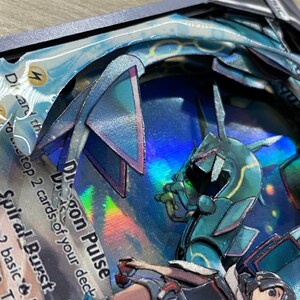 May include: A holographic Pokemon card with a blue and green dragon creature. The card is titled 'Dragon Pulse' and has the text 'Discard the top 2 cards of your deck.' The card also has the text 'Spiral Burst' and 'This attack does 2 basic Energy.' The card is displayed on a textured, brown surface.