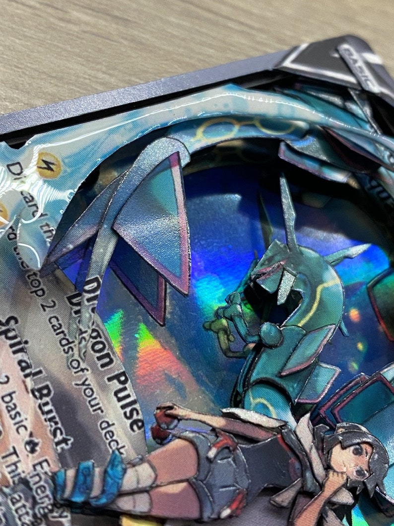 May include: A holographic Pokemon card with a blue and green dragon creature. The card is titled 'Dragon Pulse' and has the text 'Discard the top 2 cards of your deck.' The card also has the text 'Spiral Burst' and 'This attack does 2 basic Energy.' The card is displayed on a textured, brown surface.