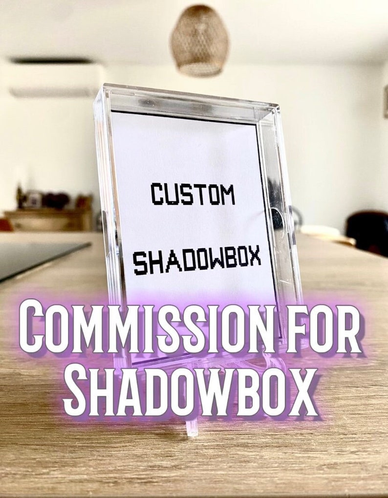 May include: A clear plastic shadow box with a white card inside. The card has the text 'CUSTOM' and 'SHADOWBOX' printed on it. The shadow box is on a wooden surface. The text 'COMMISSION FOR SHADOWBOX' is printed in purple on the image.