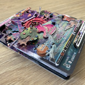 May include: A G-Max Swallow VMAX Pokemon card with a purple, pink, and green illustration. The card has a black border and features the text 'G-Max Swallow Up 2' and 'This Pokemon does -3 damage to itself and Paralyzes itself.' The card also has a VMAX rule that reads: 'When your Pokemon VMAX is Knocked Out, your opponent takes 2 Prize cards.'