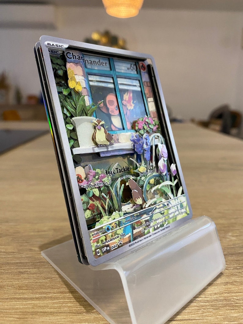May include: A Pokemon trading card featuring Charmander, a fire-type Pokemon. The card is a 3D pop-up card with a detailed illustration of Charmander looking out of a window. The card has a silver background with a blue border. The card's text reads 'BASIC', 'Charmander', '60', 'Tackle', 'This Pokemon does 10 damage to itself', 'Weakness', '6x2', 'Resistance', 'Retreat', 'SVP 044', '©2023 Pokemon / Nintendo / Creatures / Game Freak.'