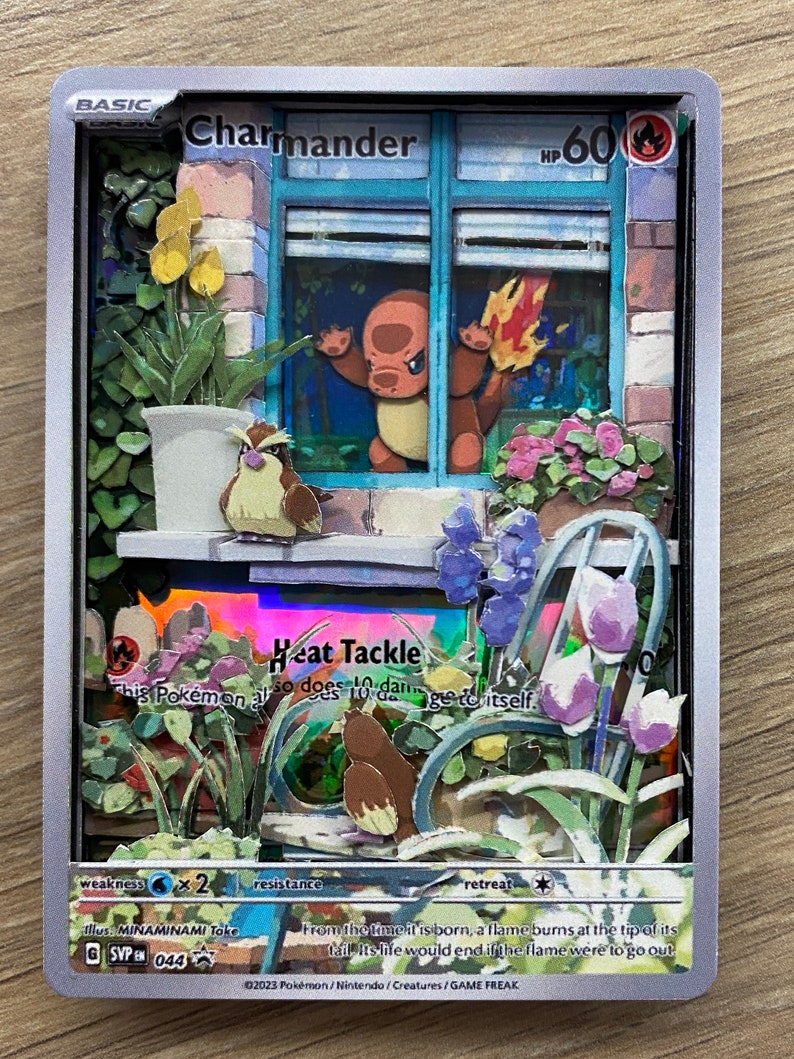 May include: Charmander Pokemon card with a silver background. The card features an illustration of Charmander looking out of a window with a potted plant and flowers. The card has a light blue border and the text 'BASIC Charmander HP 60' at the top. The card also has the text 'Heat Tackle' in a blue box with a red flame icon. The text below the attack reads 'This Pokemon also does 10 damage to itself.' The card has a weakness of water, a resistance of none, and a retreat cost of one colorless energy. The card also has the text 'From the time it is born, a flame burns at the tip of its tail. Its life would end if the flame were to go out.' The card is illustrated by MINAMINAMI Toke and has the number 044.