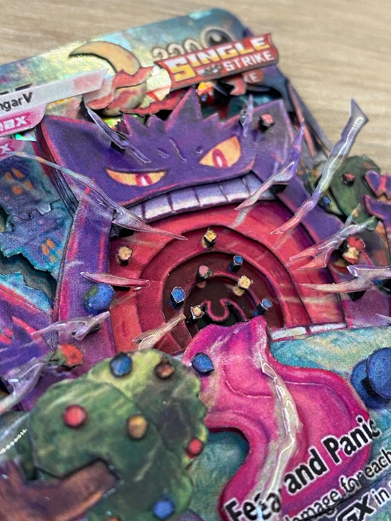May include: A Pokemon card featuring a purple and red Gengar with a single strike attack called 'Fear and Panic.' The card has a holographic finish and a background of green and pink.