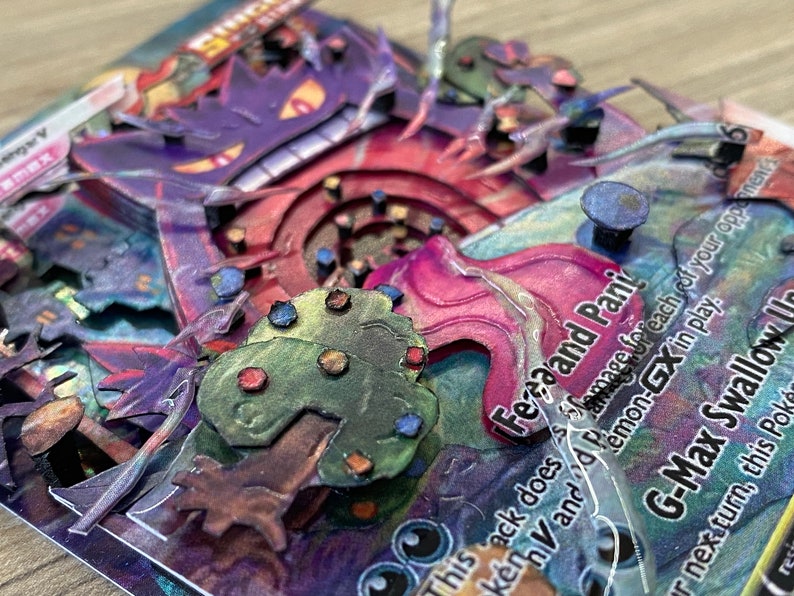 May include: A close-up of a G-Max Swallow Pokemon card with a 3D pop-up effect. The card features a purple and red Gengar with a pink and white swirl behind it. The card text reads 'Feraand Pani' and 'This attack does 30 damage for each of your opponent's Pokemon-GX in play. G-Max Swallow: During your next turn, this Pokemon can't attack.'