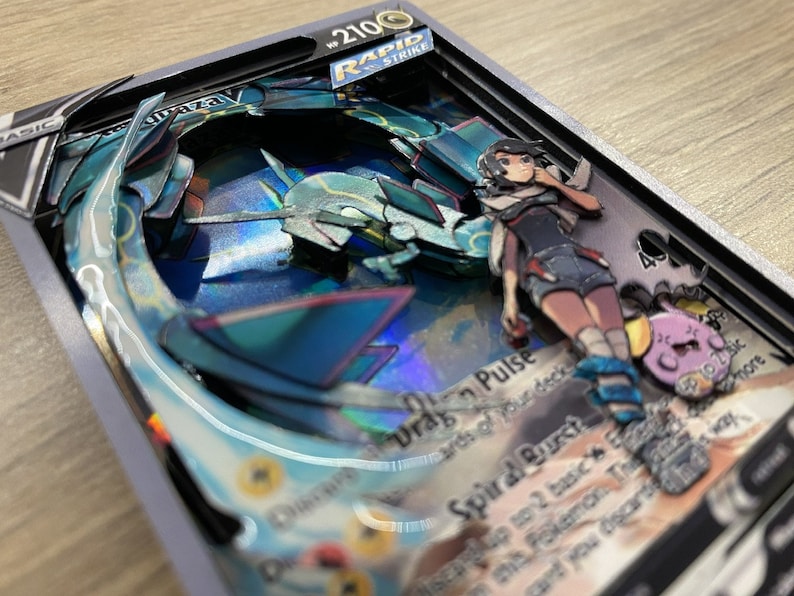 May include: A Pokemon card with a blue and silver holographic design. The card features a character with pink hair and a blue and white outfit. The card text reads 'Drag Pulse' and 'Spiral Burst'. The card is framed in a black and silver frame. The card is part of the Rapid Strike series.