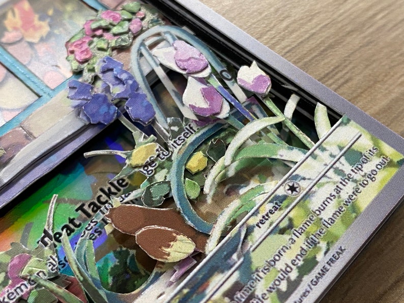 May include: A close-up of a Pokemon card with the text 'Heat Tackle' and 'retreat' visible. The card features a 3D pop-up design with flowers and leaves in shades of green, blue, and purple.