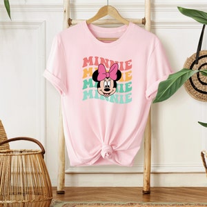 May include: Pink t-shirt with a graphic of Minnie Mouse's face and the word "Minnie" repeated in a rainbow pattern.