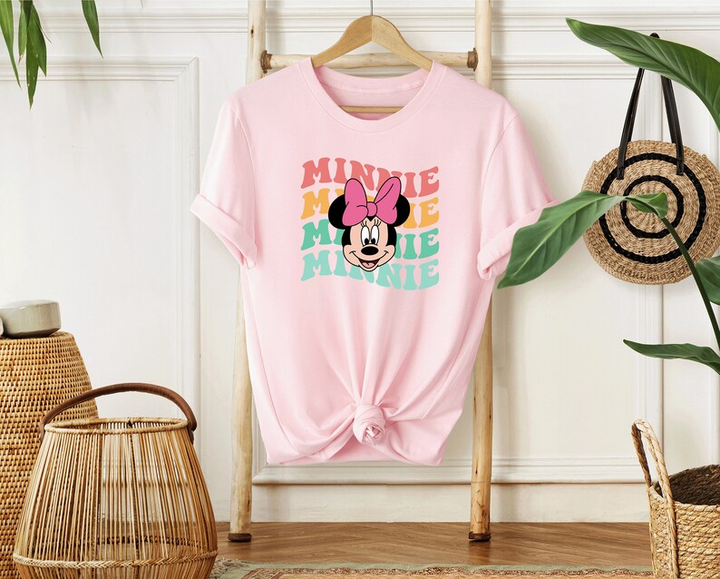 May include: Pink t-shirt with a graphic of Minnie Mouse's face and the word "Minnie" repeated in a rainbow pattern.